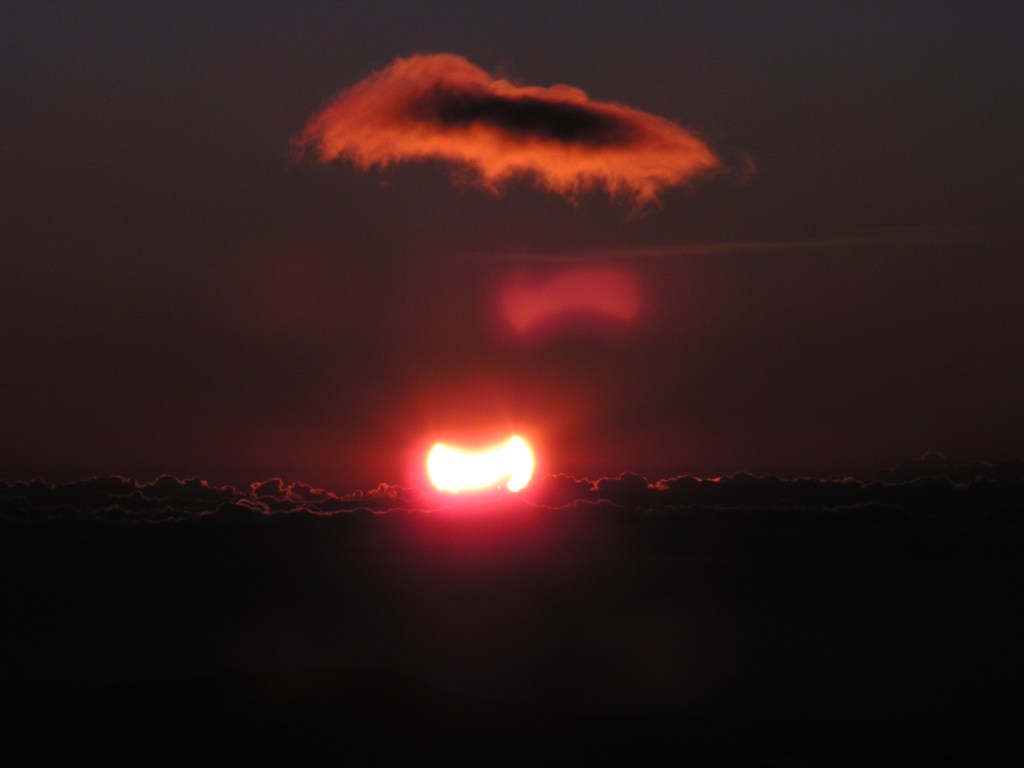 A sun partially covered by the moon rises behind a sea of ​​clouds. Without a solar filter, the sun is very bright despite the partial coverage. View from Calar Alto, Spain